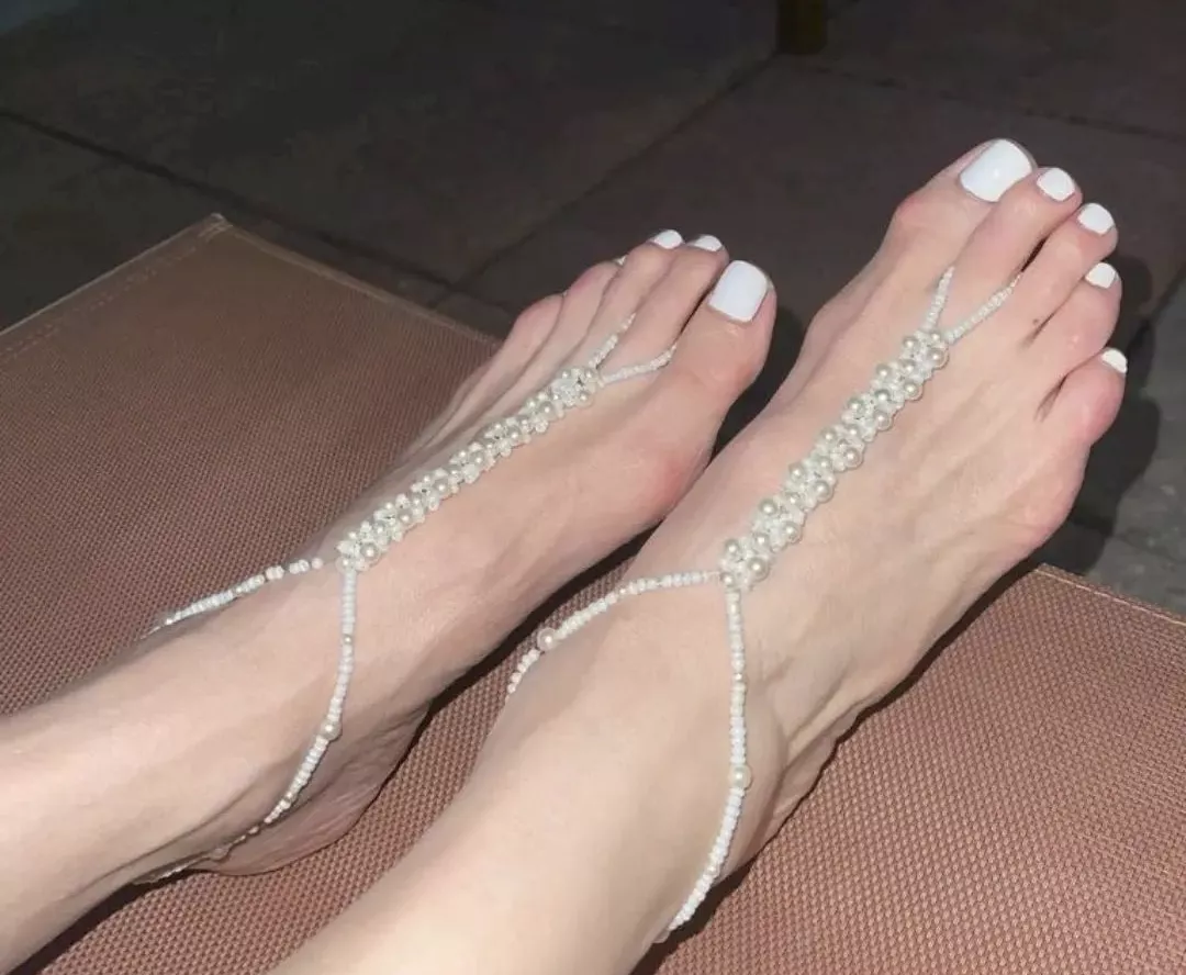 White polish with white foot jewelry adorn slender feet.