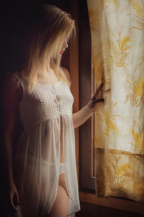 Blonde looking out the window wearing a white babydoll