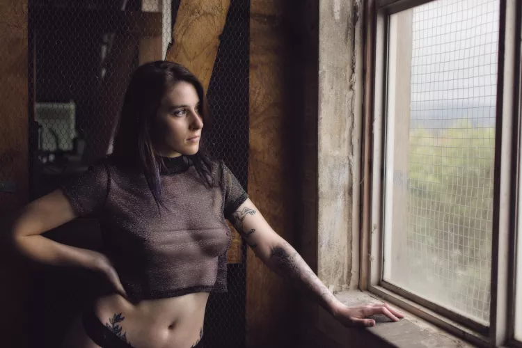 Contemplative Grace: Model in Sheer Top Against Rustic Backdrop