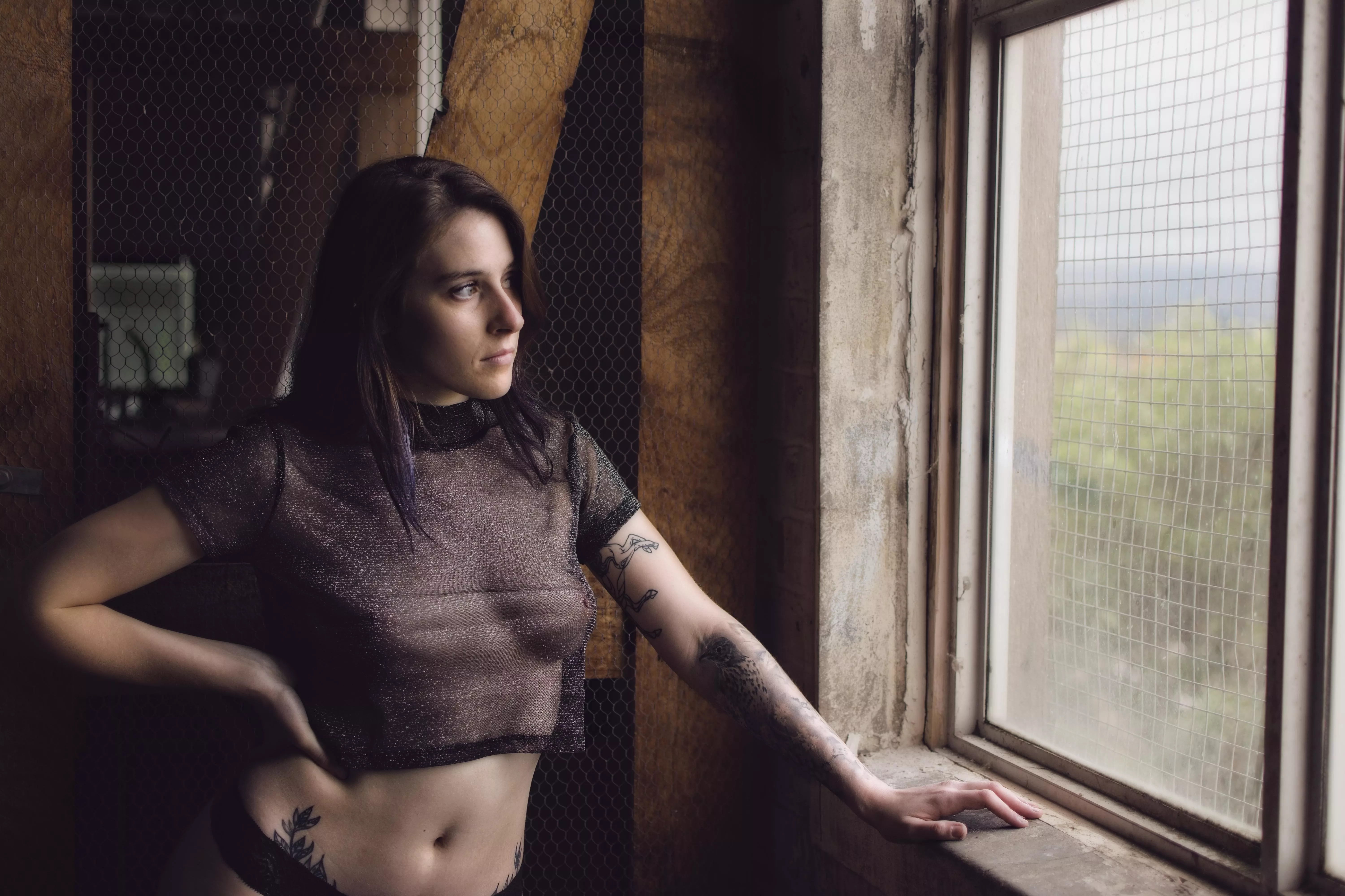 Contemplative Grace: Model in Sheer Top Against Rustic Backdrop
