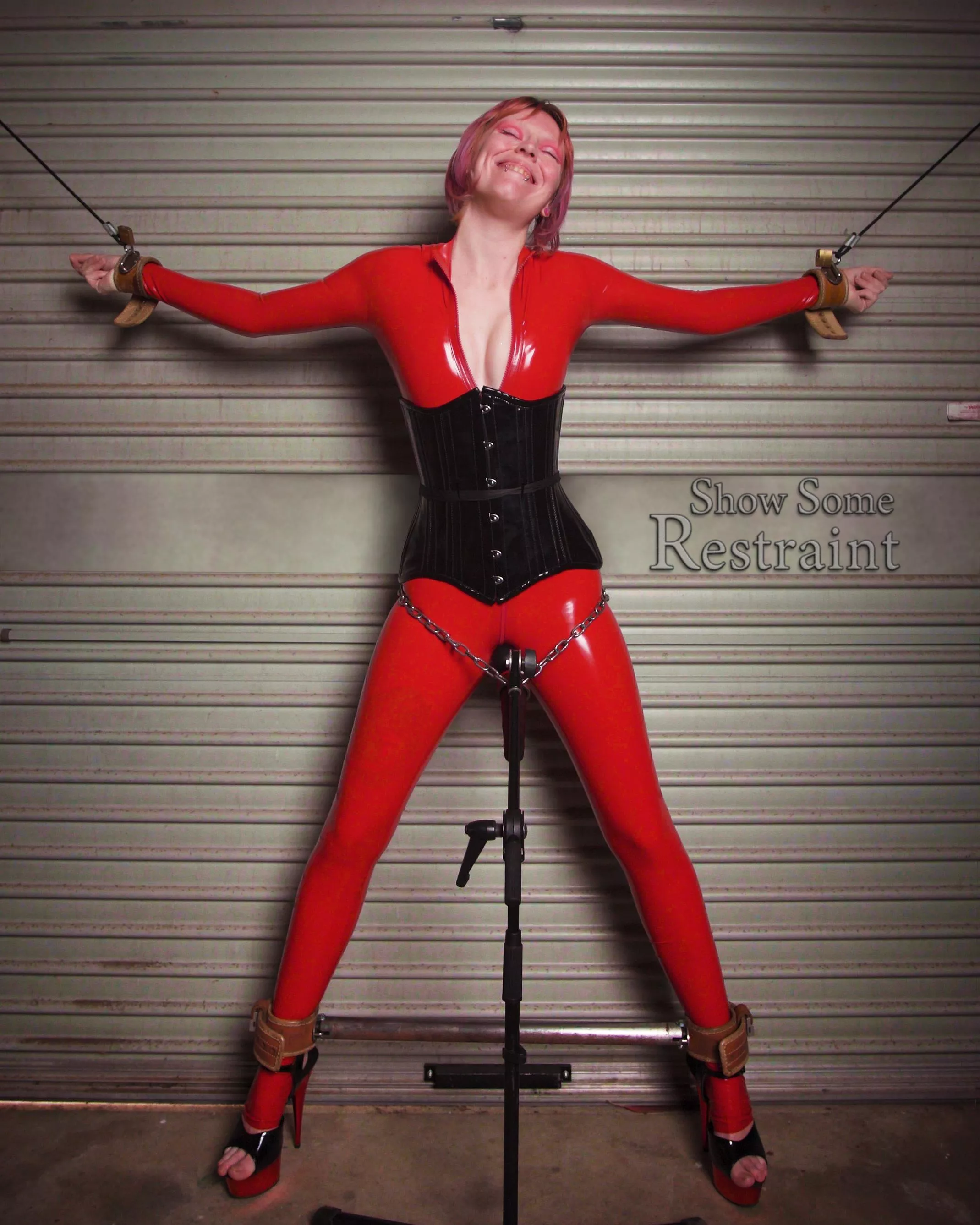 Foxxy spread out in the Humane Restraint cuffs and red latex